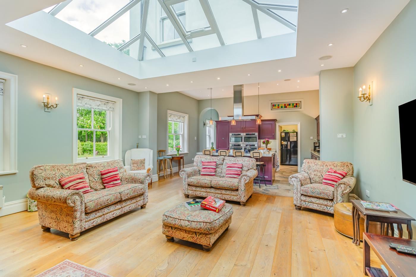A spacious living room with a high ceiling and skylight, featuring patterned sofas and a wooden coffee table.