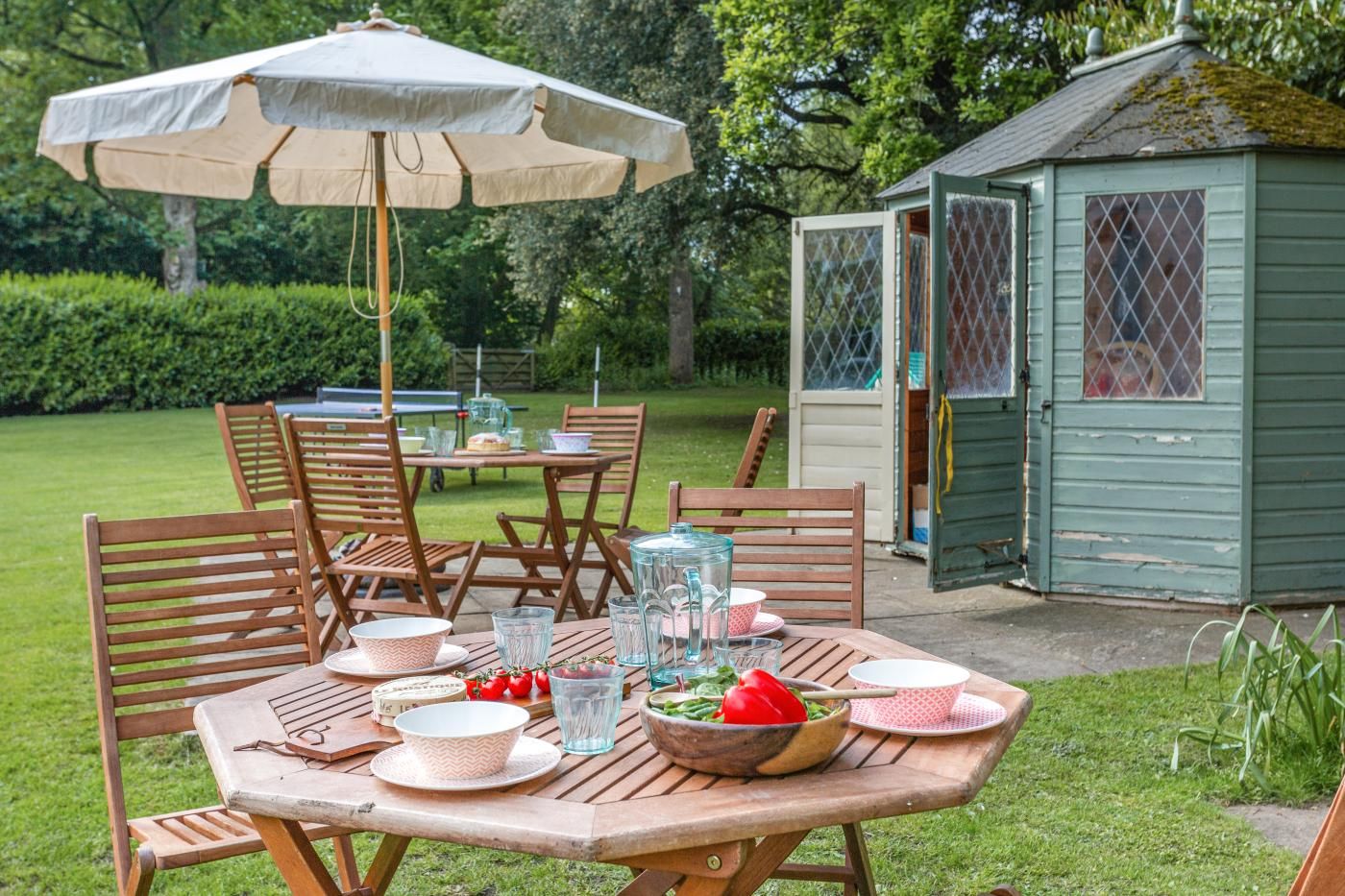 Un espace extérieur aménagé pour les repas, avec une table en bois, des chaises et un grand parasol.