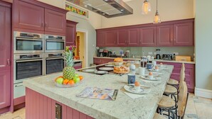 A kitchen with built-in ovens, a large island with fruit and eggs, and a dining area with chairs. - 4 Bed in York (oc-55738) (Elvington)