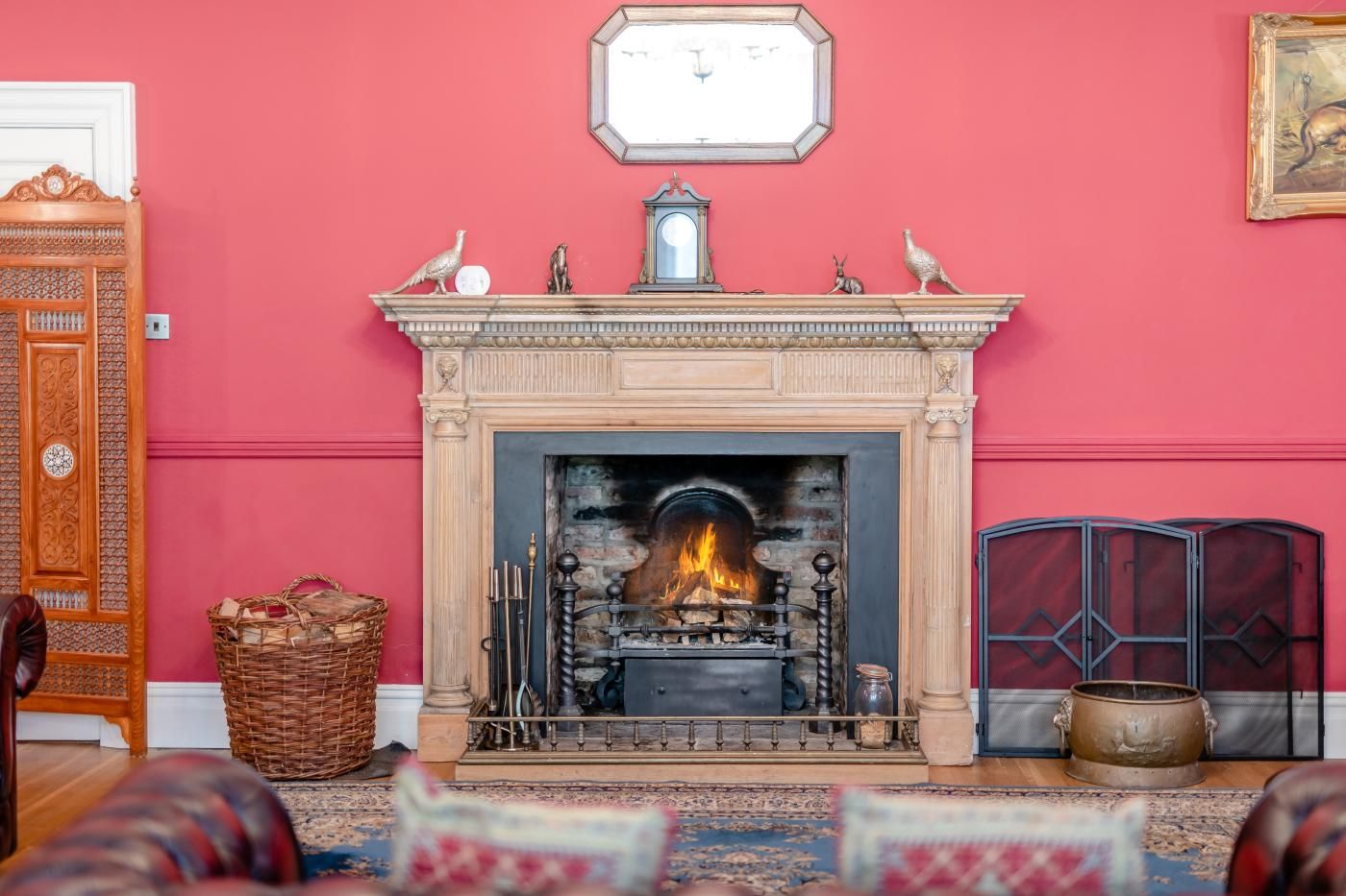 A fireplace with a fire, a clock above it, and a red wall.