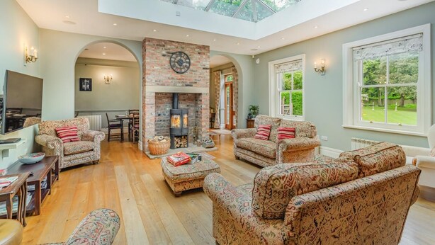 A spacious living room with a fireplace, patterned sofas, a dining area, and a skylight. - 4 Bed in York (oc-55738) (Elvington)