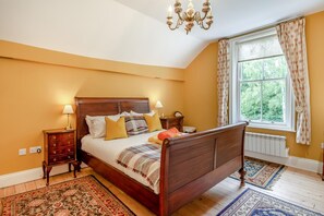 A bedroom with a wooden bed, two bedside tables, a chandelier, a window with curtains, and a radiator. - 4 Bed in York (oc-55738) (Elvington)