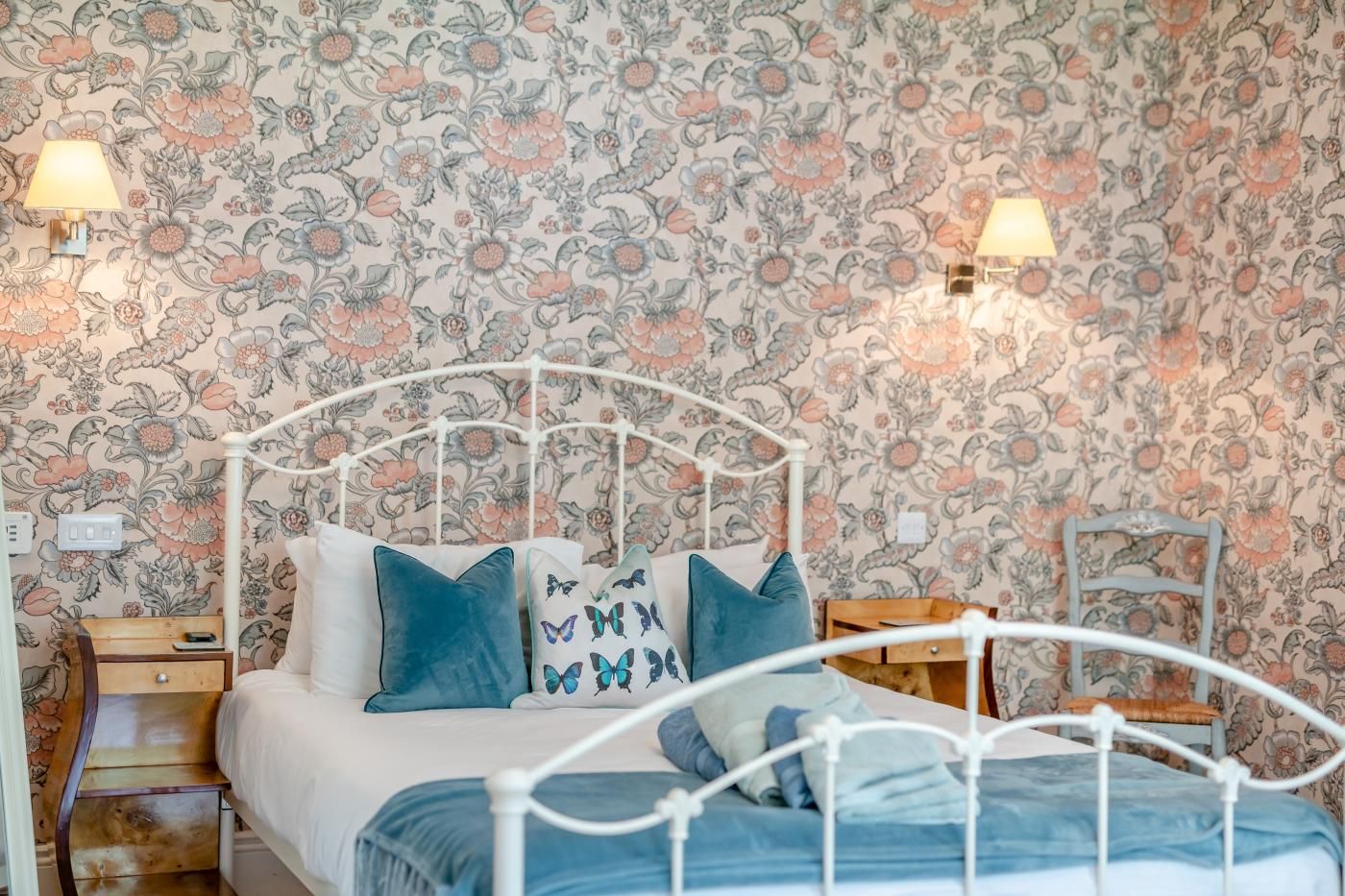 A bed with a white metal frame, blue bedding, and decorative pillows with butterfly patterns.