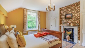 A bedroom with a bed, a chandelier, a window with curtains, a fireplace, and a patterned wall. - 4 Bed in York (oc-55738) (Elvington)