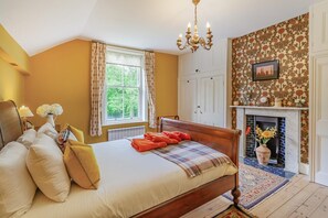 Ein Schlafzimmer mit einem Bett, einer Chandelüster, einem fenster mit Vorhängen, einem Kamin und einer Wand mit Muster.