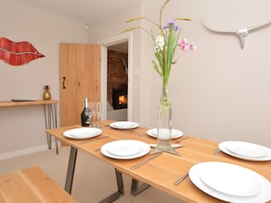 Un coin repas avec une table en bois dressée pour six personnes, un vase rempli de fleurs et une cheminée en arrière-plan.