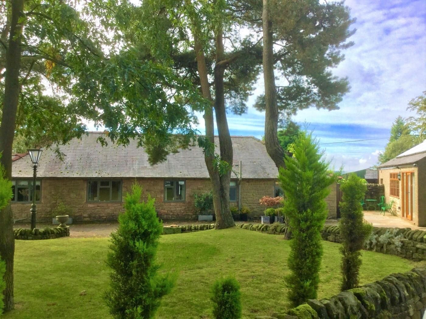 Un bâtiment en pierre avec une cour verdoyante, un mur en pierre et un petit jardin agrémenté d’arbustes.