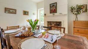 A dining room with a wooden table set for a meal, surrounded by chairs, with a fireplace and wall-mounted pictures. - 4 Bed in Lyndhurst (oc-57407) (Lyndhurst)