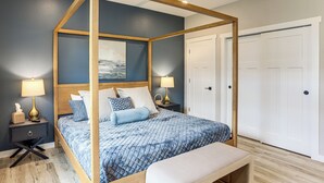 Un lit à baldaquin avec une couvre-lit bleue à motifs, des lampes de chevet, une table de chevet avec une lampe et un banc au pied du lit.