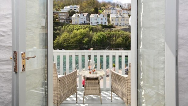 Ein Balkon mit Korbstühlen und einem Tisch, mit Blick auf ein Wohngebiet mit Häusern und Grünflächen.