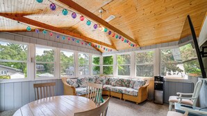 A sunroom with a wooden ceiling, large windows, a round table, and a built-in sofa. - Stroll to Shore! Michigan City Family Getaway (Michigan City)