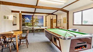 Ein Billardtisch mit grüner Spielfläche, Holzstühle und ein Tisch mit weißer Tischdecke.