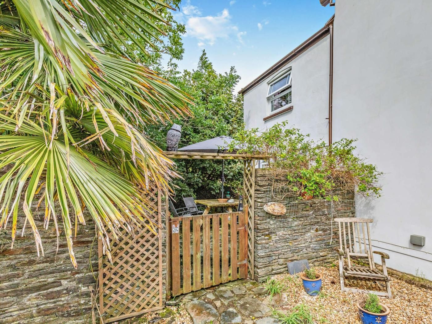 Un patio con un portón de madera, un muro de piedra y una pérgola con una mesa y sillas.