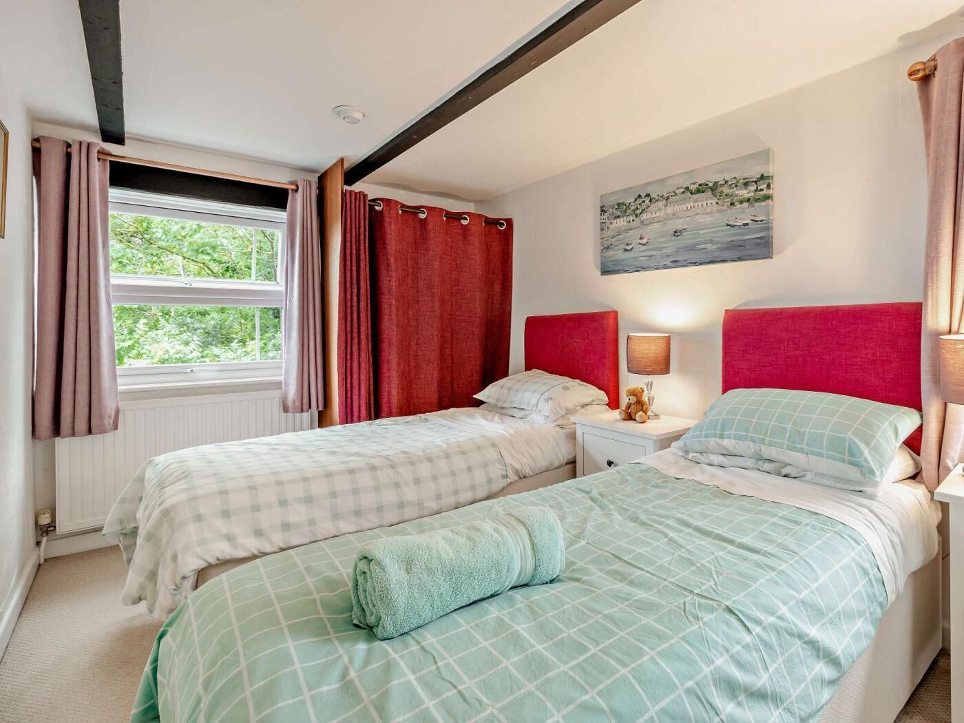 Una camera da letto con due letti, una finestra con tende, un quadro al muro e un comodino con una lampada.