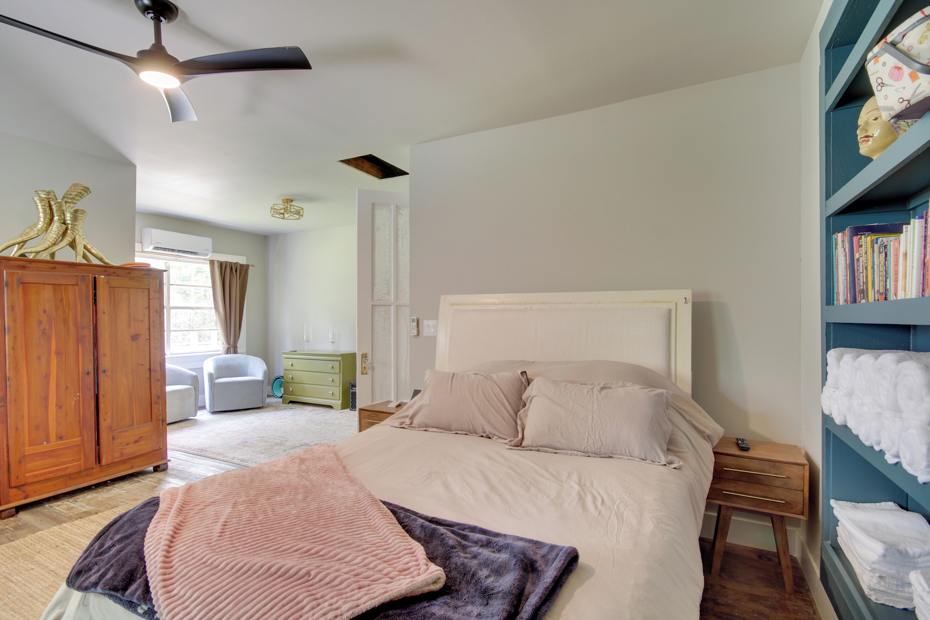Un dormitorio con cama, armario, mesita de noche, estantería y ventilador de techo.