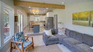 A modern living room with a grey sectional sofa, a wooden chair, and a large window. - Private Ocean Springs Waterfront Retreat w/Porch (Ocean Springs)