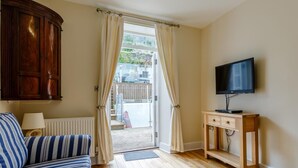 Ein Zimmer mit einem Holzkasten, einem gestreiften Sofa, einem Fernseher auf einem Holzboden und Blick durch eine Tür.