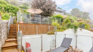 Eine Holzterrasse mit Liegestühlen und einem Glasgeländer mit Blick auf einen Garten.