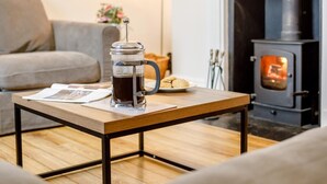 Ein gemütliches Wohnzimmer mit einer Kaffeemaschine auf einem Holztisch, einer Couch und einem Kamin im Hintergrund.