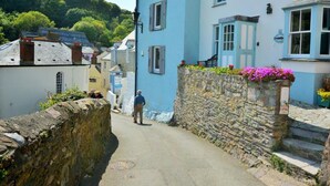 Eine schmale Gasse mit Steinwänden, ein blaues Gebäude mit einem Schild und eine Person, die unterwegs ist.