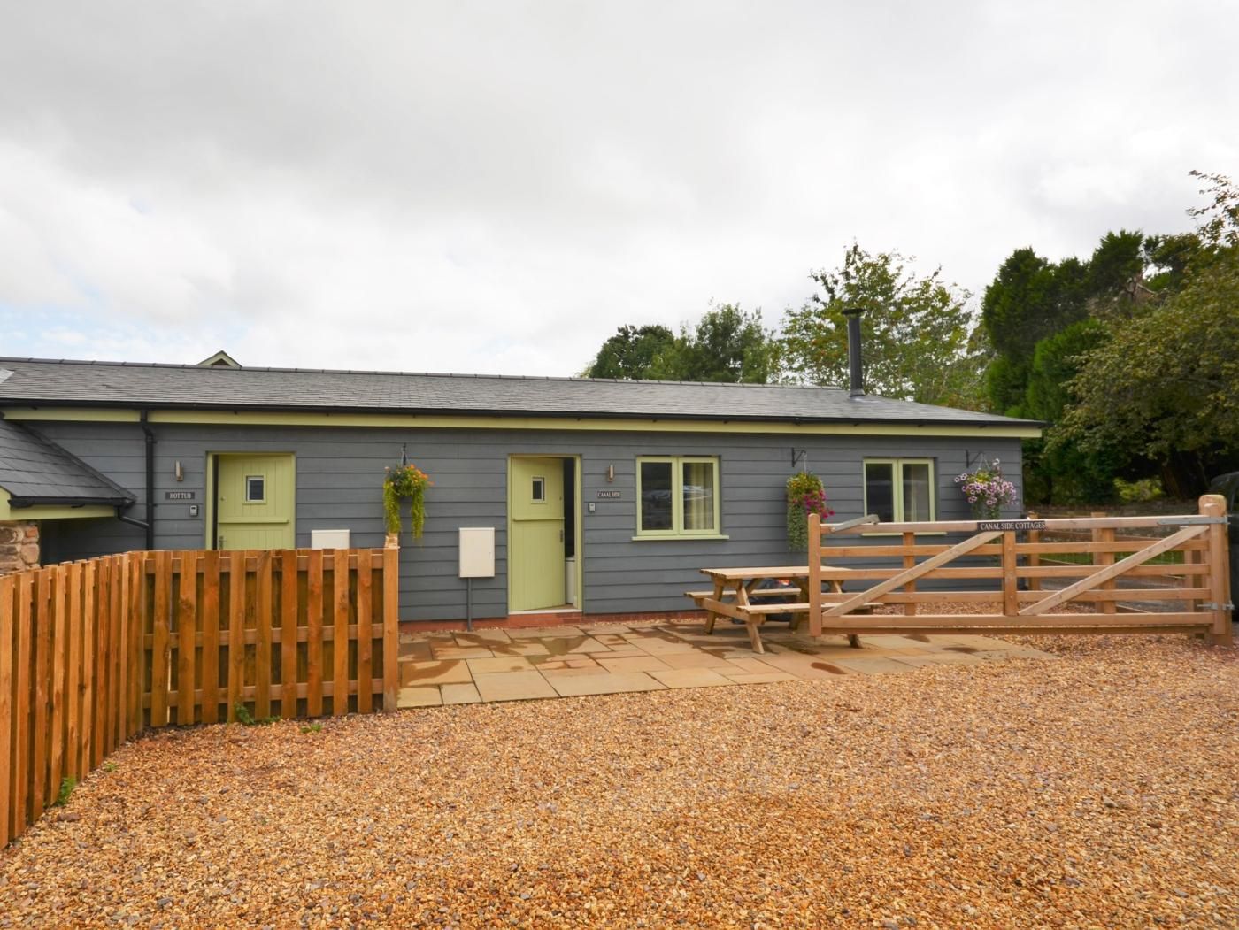 A cottage with a gravel driveway, wooden fence, and a wooden gate.