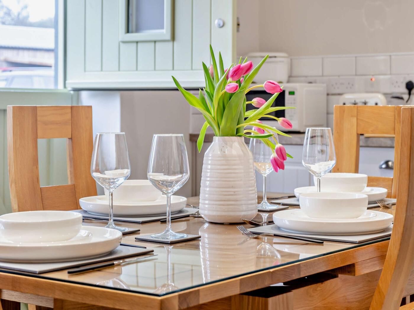 A dining table set with white plates, glasses, and a vase with flowers.