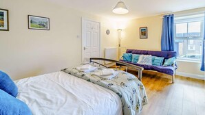 Ein Schlafzimmer mit einem Bett, einem Sofa, einem Fenster mit Vorhängen, einer Tür und an der Wand hängenden Bildern.
