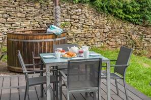Ein Essbereich im Freien mit einer Steinsandsteinwand im Hintergrund, einem Holzfass und einem für das Frühstück gedeckten Tisch.