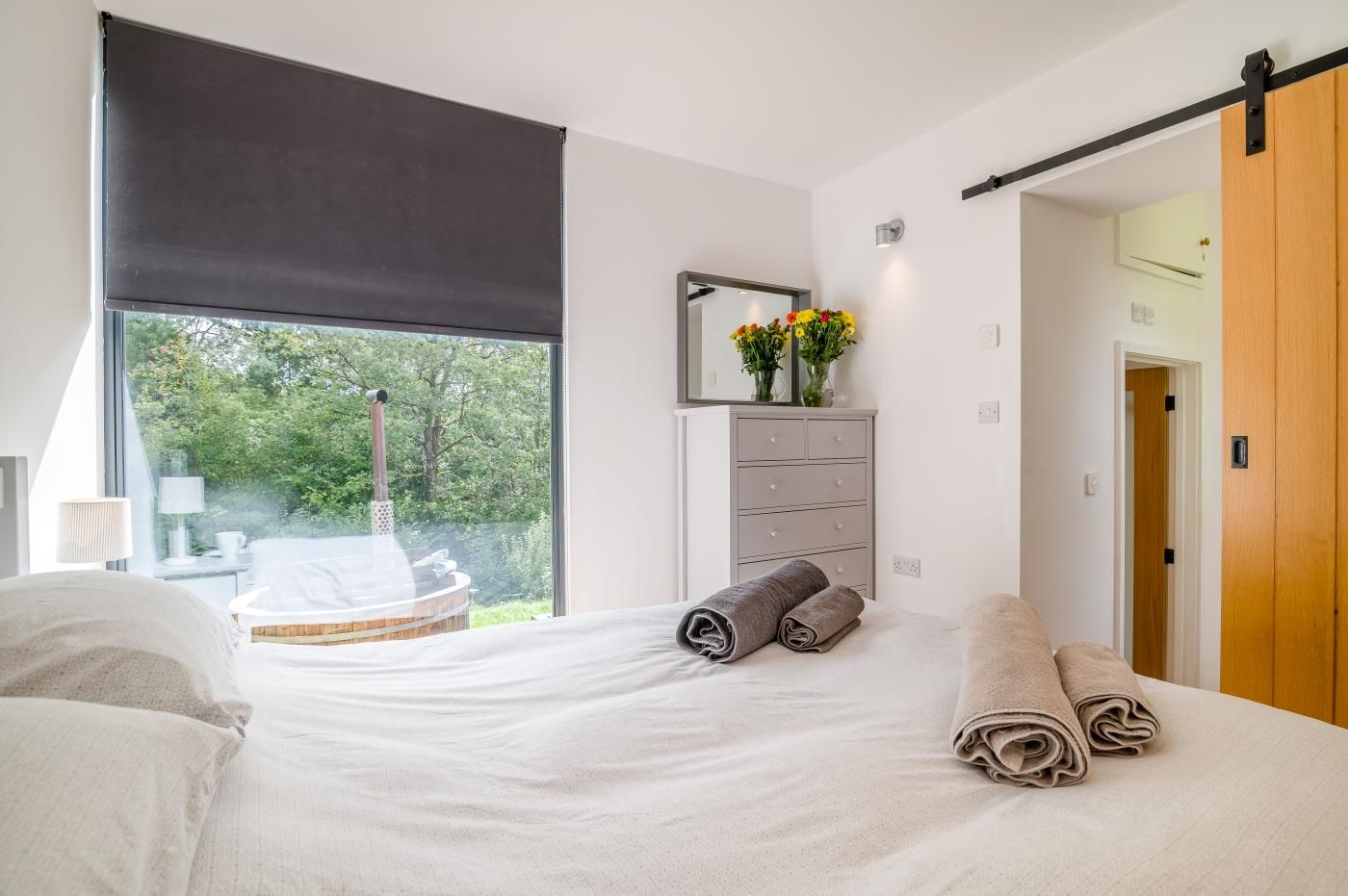 A bedroom with a bed, a window with a view of greenery, a heater, and a dresser with towels.