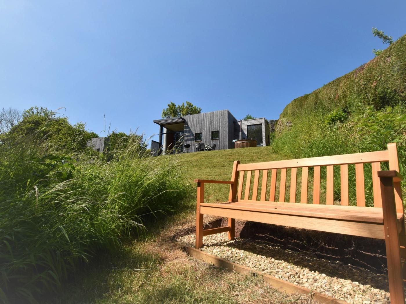A modern building with a sloped roof, a wooden bench, and a grassy hill.