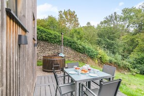 An outdoor patio with a stone wall, a wooden hot tub, and a table set for a meal.
