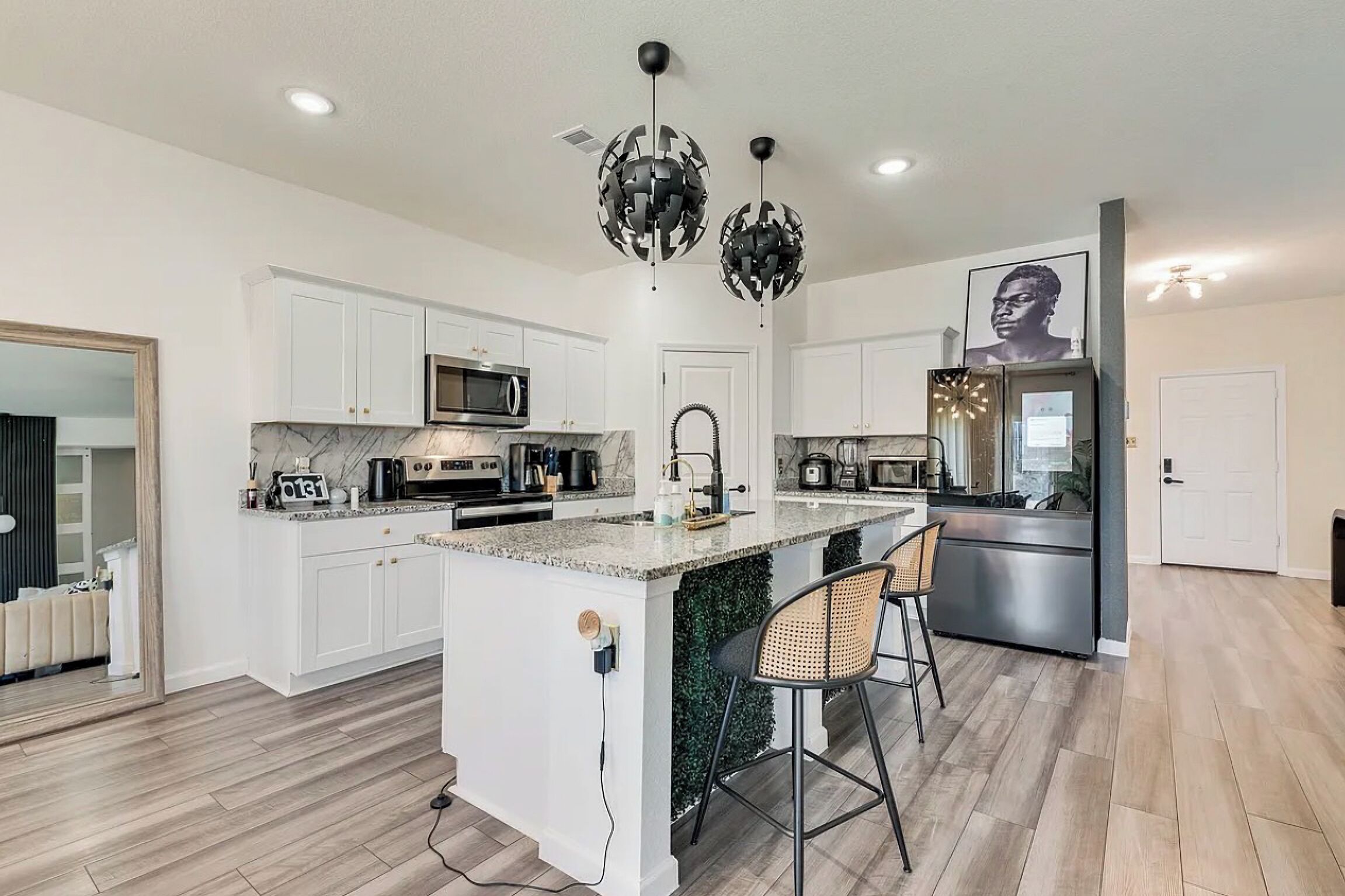 A modern kitchen with white cabinets, a marble countertop, stainless steel appliances, and a central island with bar stools.