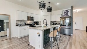 A modern kitchen with white cabinets, a marble countertop, stainless steel appliances, and a central island with bar stools. - Great for Families! Glenn Heights Getaway w/ Yard (Glenn Heights)