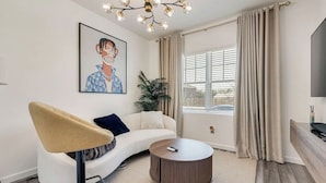 A modern living room with a sofa, a round coffee table, a painting, a plant, and a large window with curtains. - Great for Families! Glenn Heights Getaway w/ Yard (Glenn Heights)