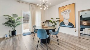 A dining area with a round table, blue chairs, a chandelier, a large painting, and a potted plant. - Great for Families! Glenn Heights Getaway w/ Yard (Glenn Heights)