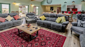 Ein großzügiger Wohnbereich mit grauen Sofas, einem Holztisch und einem roten Teppich mit Muster.