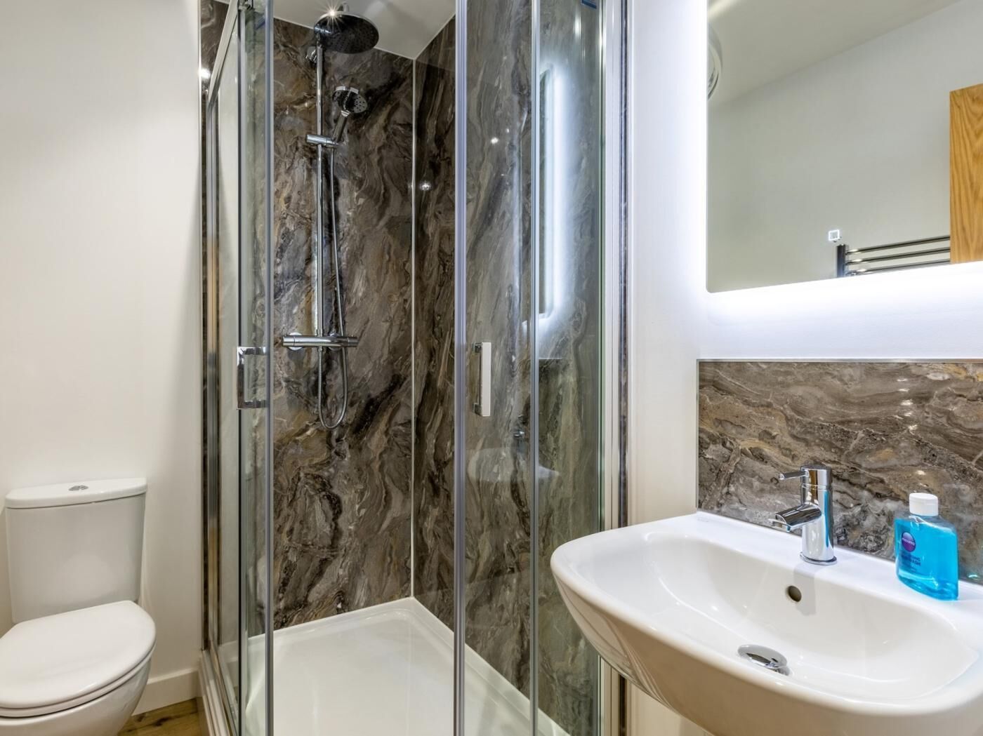 A bathroom with a glass-enclosed shower, a white toilet, and a sink with a marble backsplash.