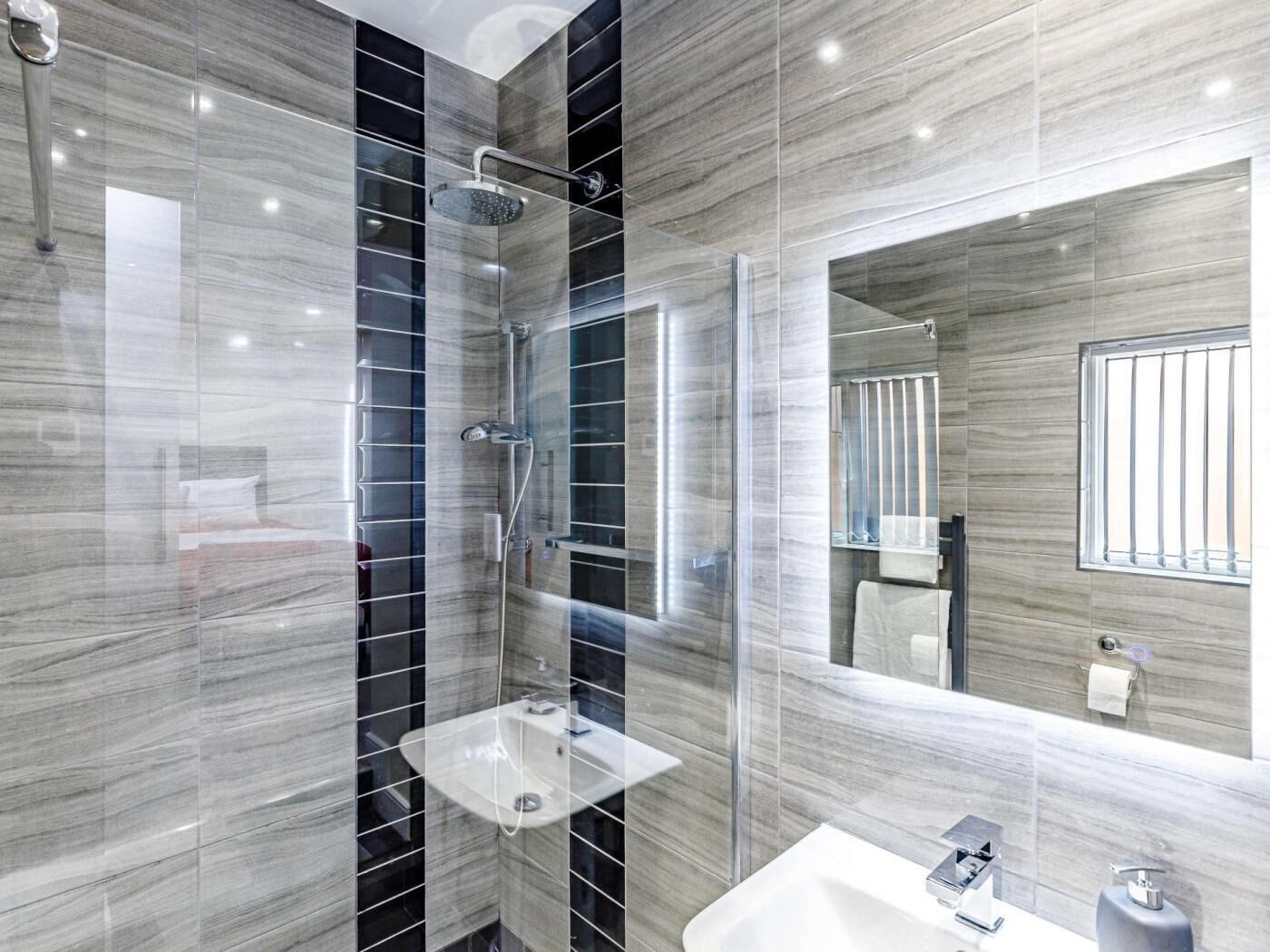 A modern bathroom with a glass-enclosed shower, a white sink, and a large mirror.