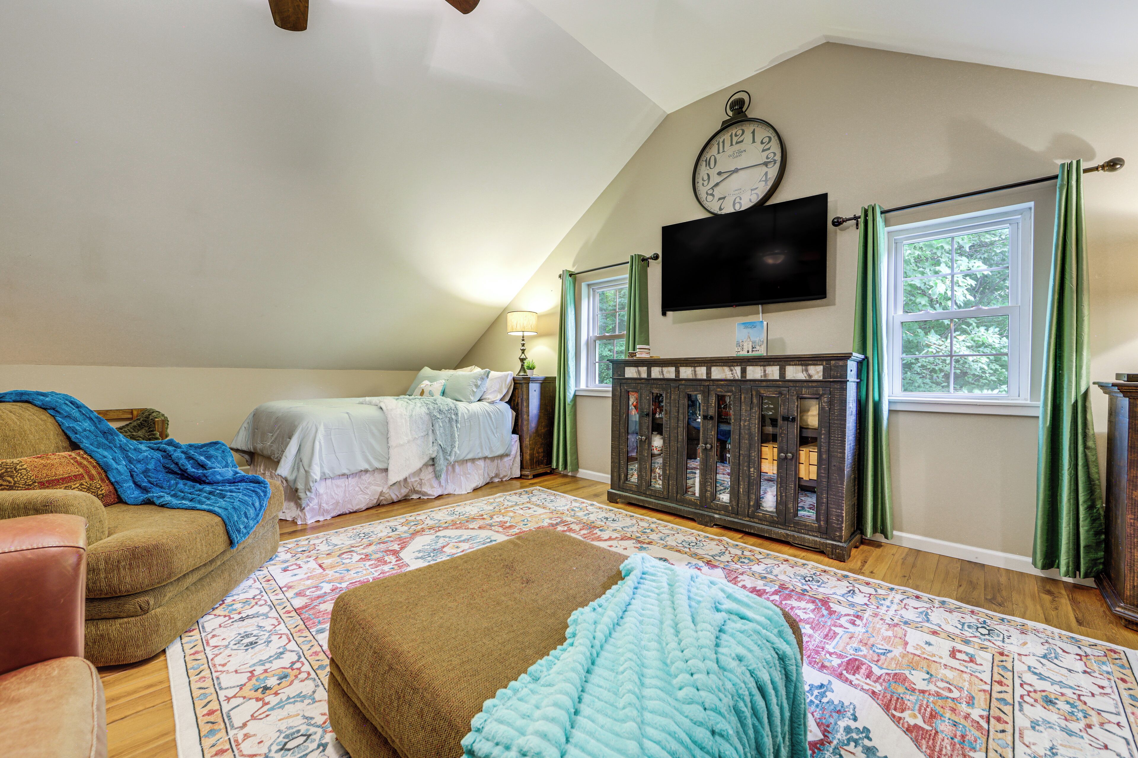A bedroom with a sloped ceiling, a bed, a sofa, a television, and a cabinet.