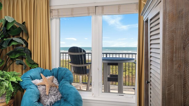 Una habitación con un ventanal grande, una silla azul, una decoración con forma de estrella de mar y vistas al océano.