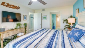 Un dormitorio con cama, ventilador de techo, televisor y una puerta que da a otra habitación.