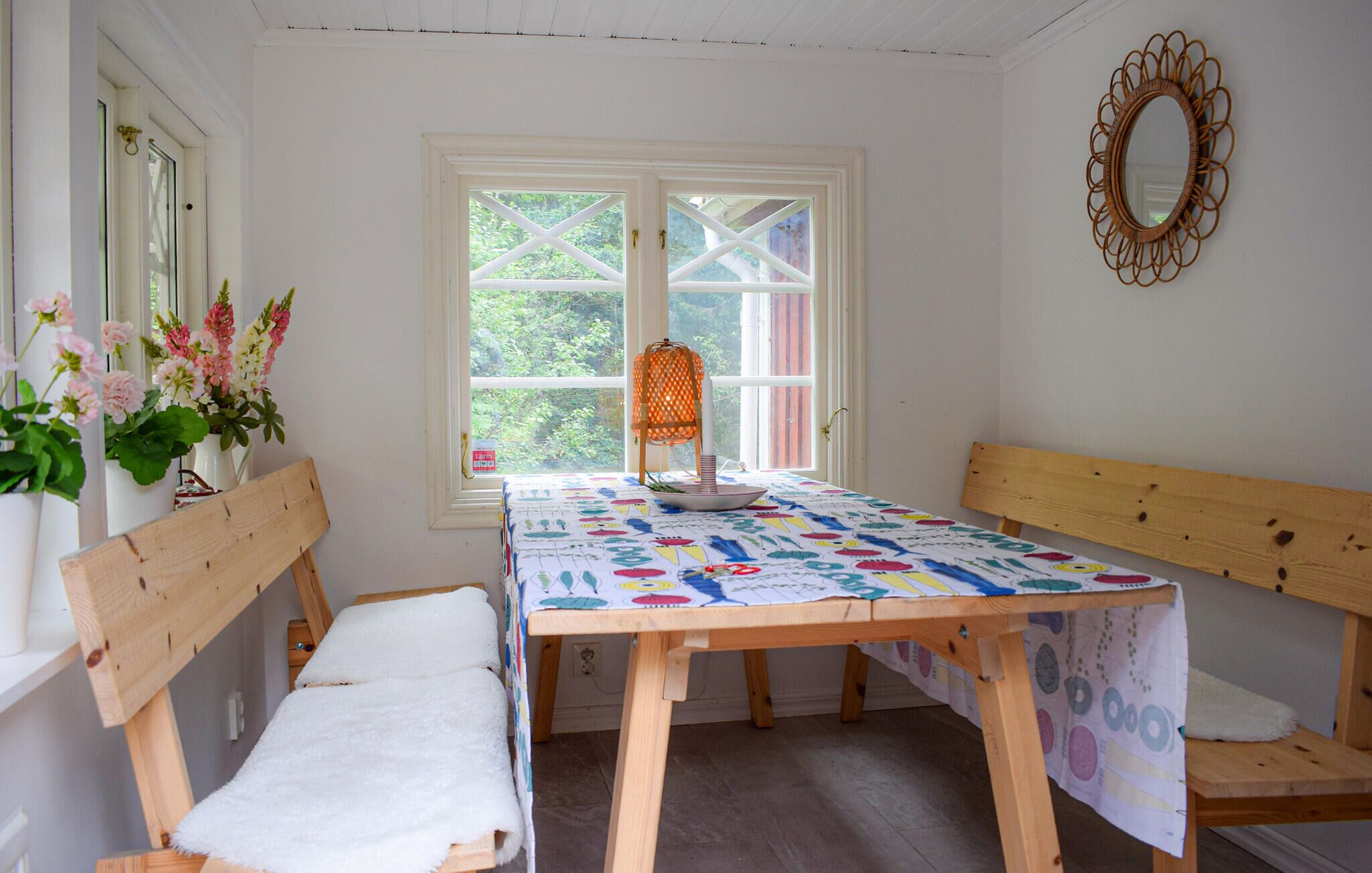 A room with a wooden table, benches, a window with a view, and a wall-mounted mirror.