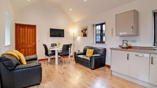 Een moderne woonkamer met een eettafel, zwarte leren bank en een keuken met kasten en waterkoker.