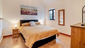 Een slaapkamer met een bed, nachtkastje, raam en een schilderij aan de muur.