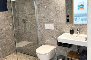 Ein modernes Badezimmer mit einer gläsernen Duschkabine, einer weißen Toilette und einem Waschbecken mit schwarzem Seifenspender.