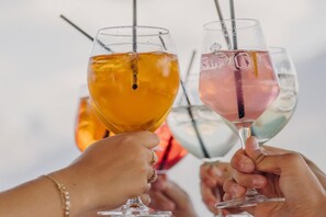 Two hands holding glasses with straws, one with a clear liquid and the other with a pinkish liquid. - Ski-in/ski-out apartment Monte Central (Neukirchen)