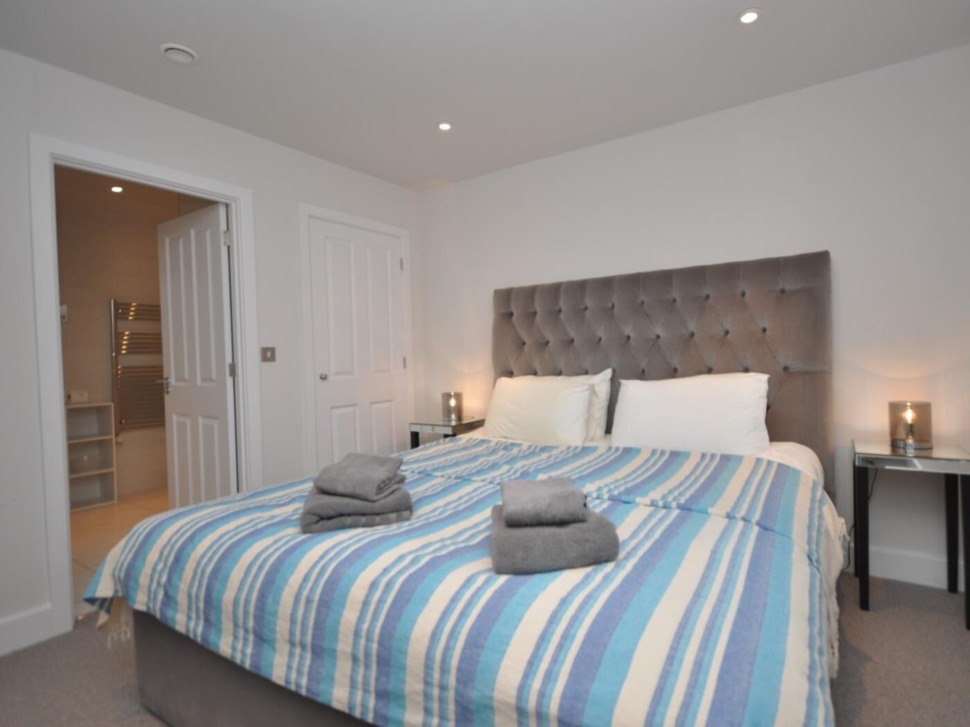 A bedroom with a large bed, a tufted headboard, bedside tables with lamps, and a walk-in closet.