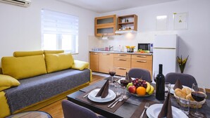 A modern living room with a yellow sofa, a dining table set with plates, glasses, and a bottle of wine. - Ota Residence Koper (Koper)