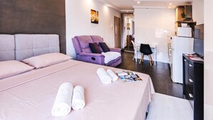 A modern hotel room with a large bed, a seating area with a sofa and armchair, a small desk with a chair, and a kitchenette. - Ota Residence Koper (Koper)