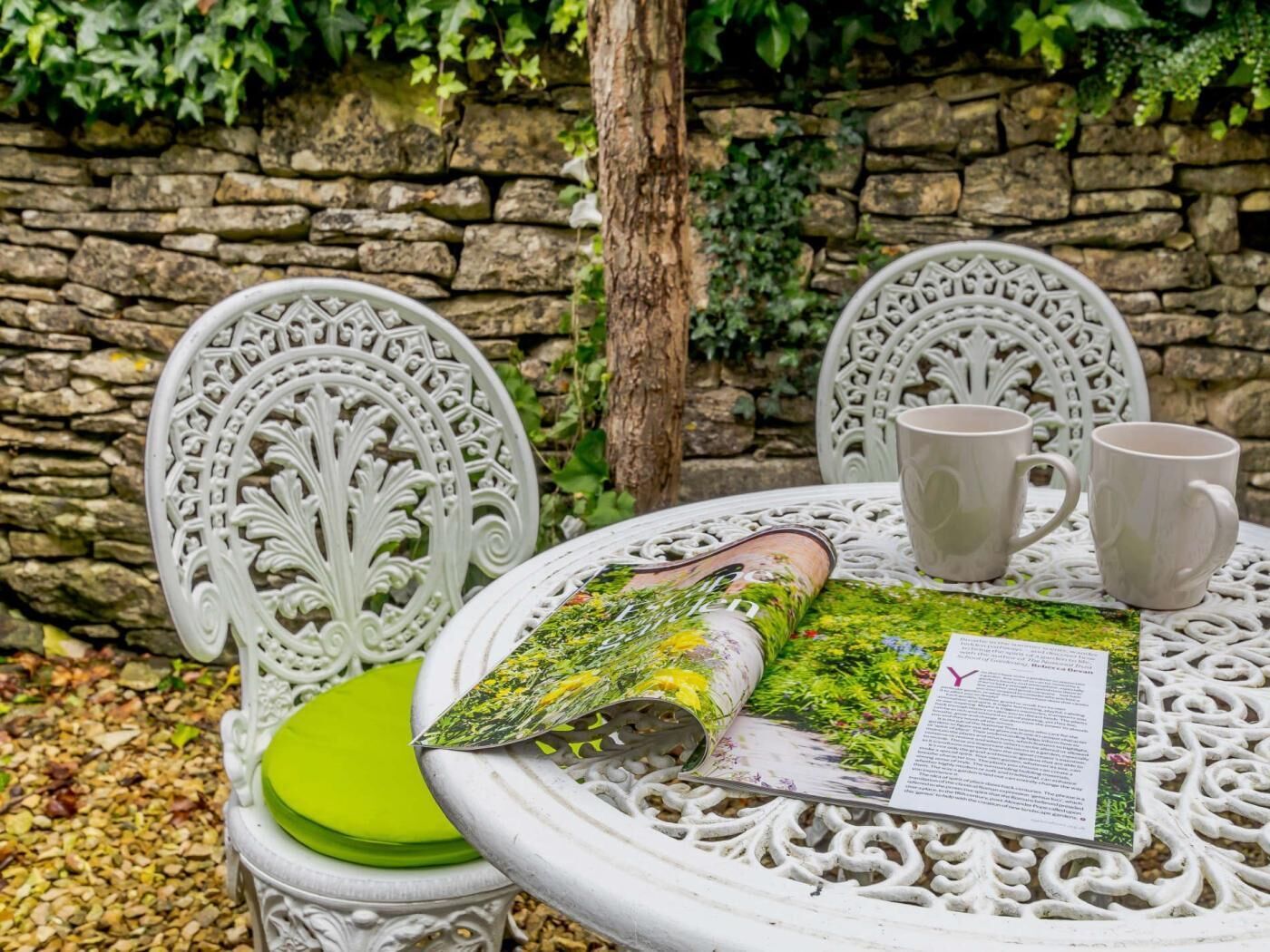A round table with a decorative white metal frame, two white ceramic mugs, and a rolled-up book with a green cover.